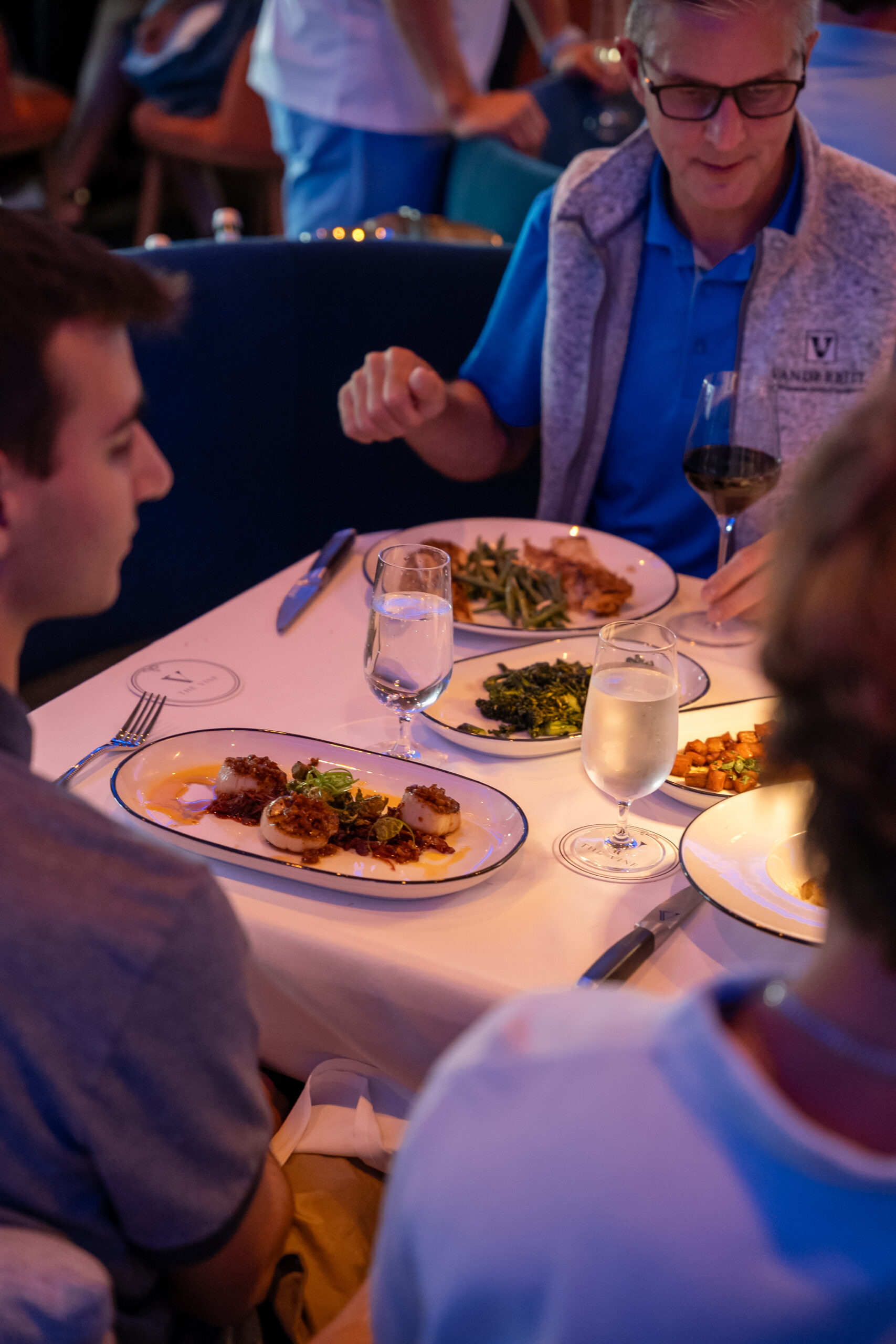 A family seated around a table with pan-fried scallops, broccolini, tableside dover sole, and wine on it