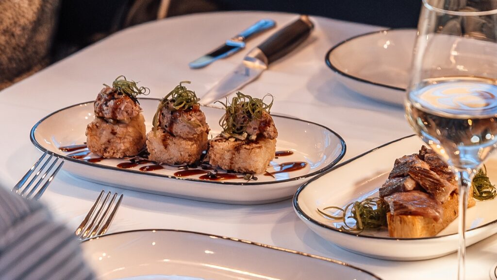 Spicy tuna on top of crispy rice with a soy glaze with wagyu on top of a fried compressed potato next to it on a beautifully set table