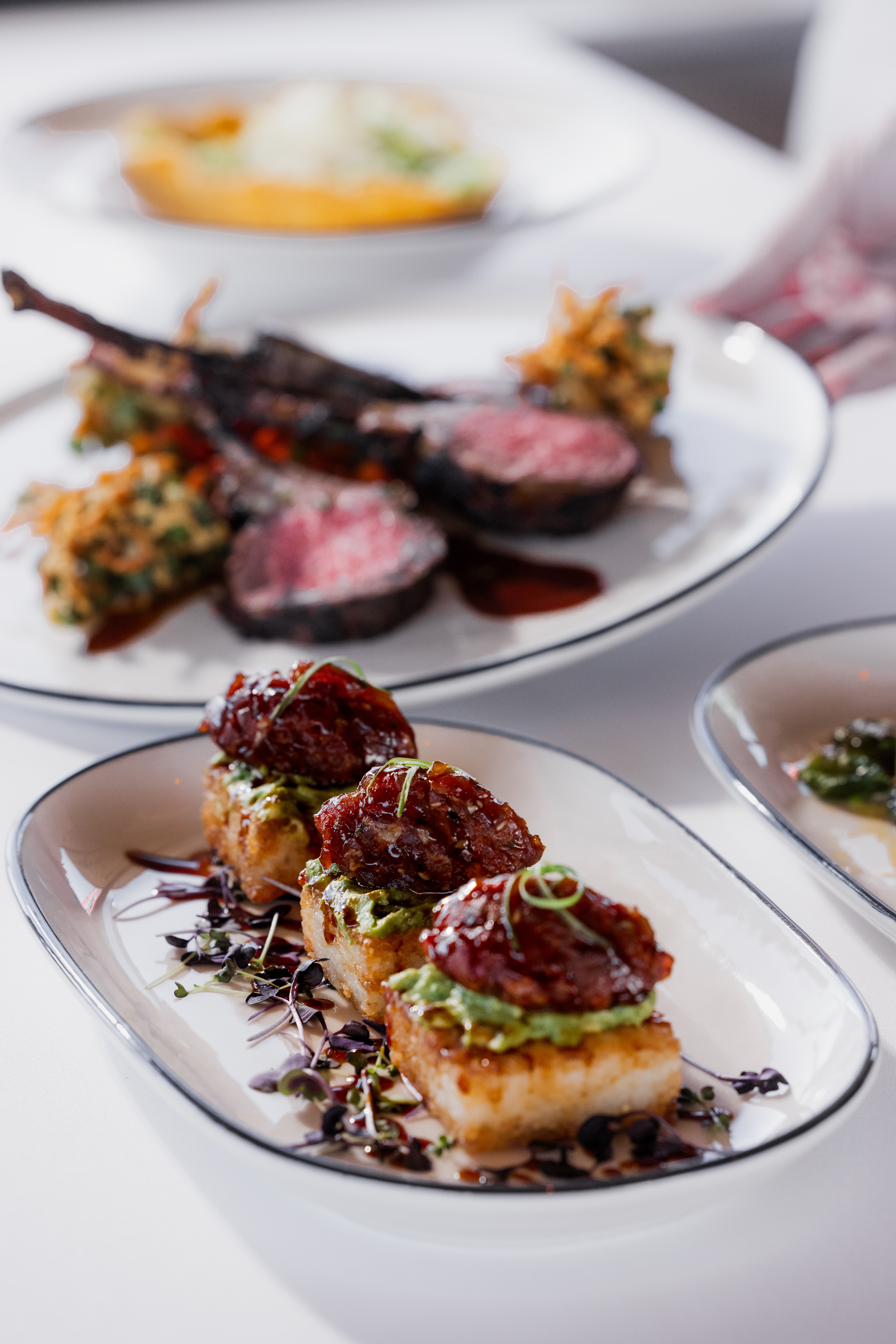 Spicy tuna with avocado on top of a crispy rice square in front of lamb chops